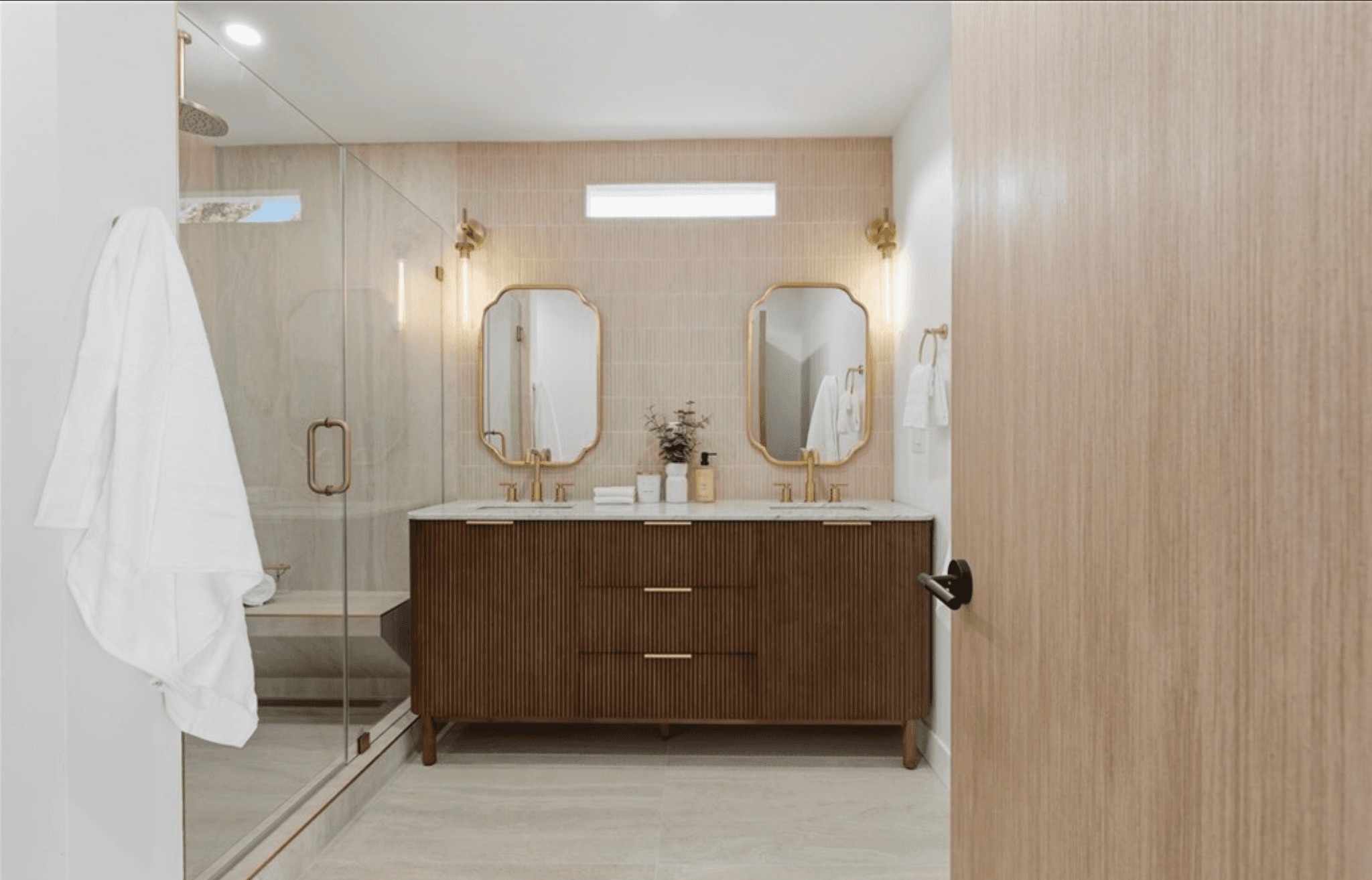 Bathroom with a fluted wood vanity, brass mirrors, and a glass shower